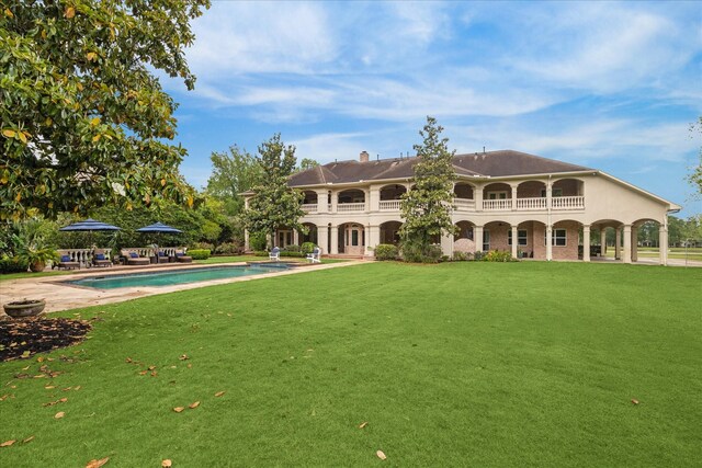 rear view of house with a patio, an outdoor pool, a yard, and a balcony