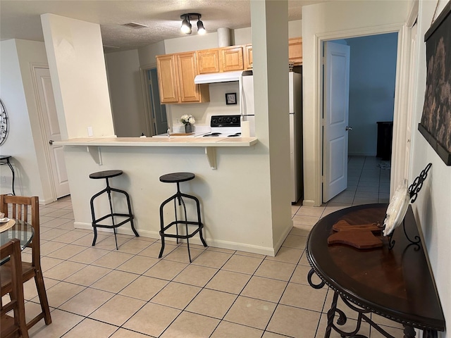 kitchen with a breakfast bar area, light brown cabinetry, electric range oven, under cabinet range hood, and light tile patterned floors
