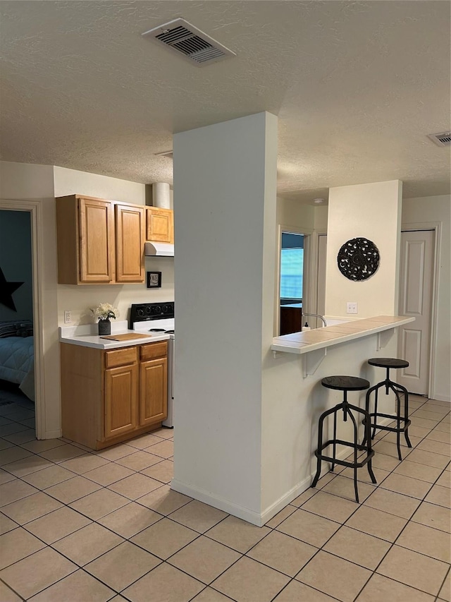 kitchen featuring a breakfast bar, white range with electric cooktop, visible vents, and light tile patterned floors