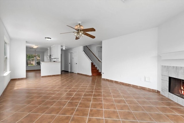 unfurnished living room with a fireplace, stairway, a ceiling fan, and baseboards