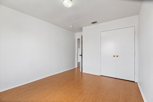 unfurnished bedroom featuring baseboards, wood finished floors, visible vents, and a closet