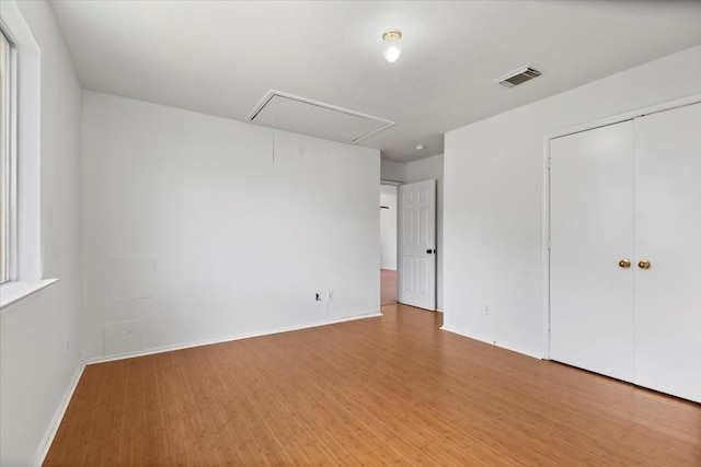 unfurnished bedroom featuring visible vents, light wood-style floors, a closet, baseboards, and attic access