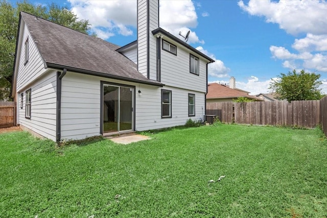 rear view of property featuring a chimney, central AC unit, a fenced backyard, a yard, and roof with shingles
