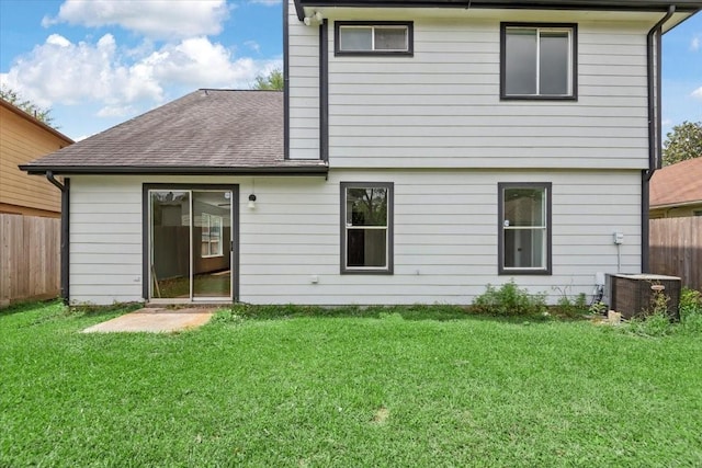 rear view of property featuring a lawn, fence, roof with shingles, and cooling unit