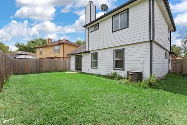 back of house featuring a fenced backyard, a chimney, a yard, and central AC