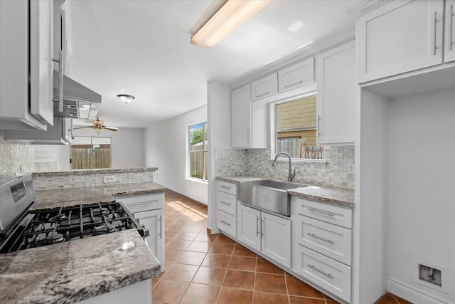 kitchen featuring stainless steel range with gas stovetop, a sink, tasteful backsplash, white cabinetry, and light tile patterned floors