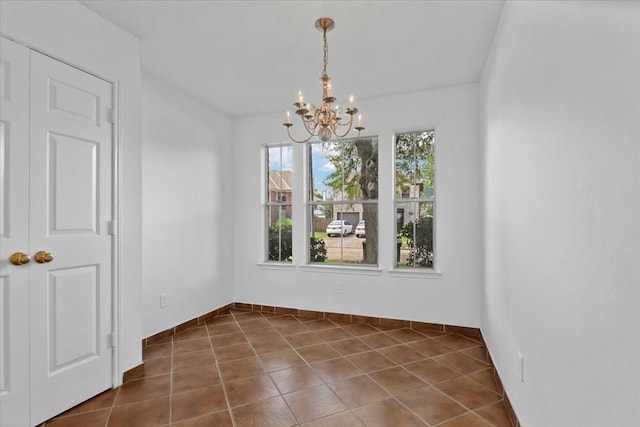 unfurnished dining area featuring a chandelier, baseboards, and dark tile patterned flooring