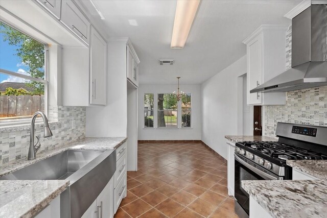 kitchen featuring wall chimney range hood, a sink, a healthy amount of sunlight, stainless steel gas range oven, and visible vents