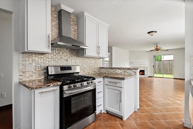 kitchen featuring stainless steel gas stove, a ceiling fan, wall chimney exhaust hood, decorative backsplash, and open floor plan