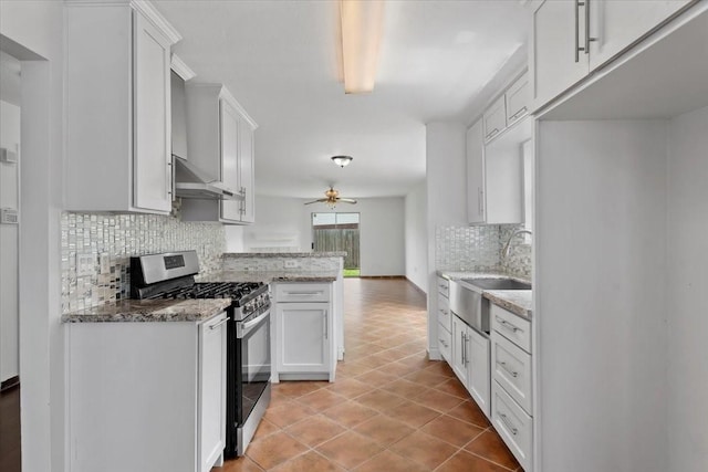 kitchen featuring a sink, decorative backsplash, a ceiling fan, wall chimney range hood, and stainless steel gas stove
