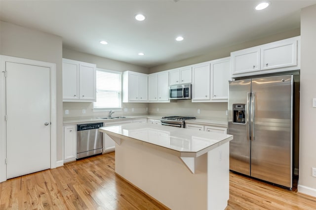 kitchen with appliances with stainless steel finishes, a kitchen island, light countertops, a sink, and white cabinetry