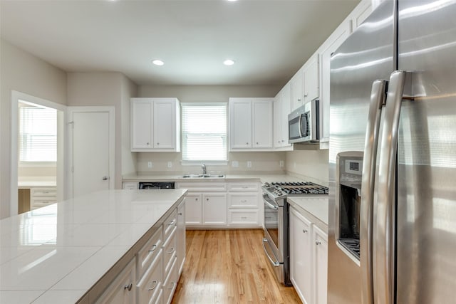 kitchen with appliances with stainless steel finishes, a sink, white cabinetry, light wood-type flooring, and tile countertops