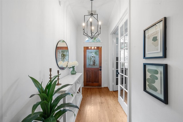 foyer entrance featuring visible vents, ornamental molding, light wood-style flooring, and a notable chandelier