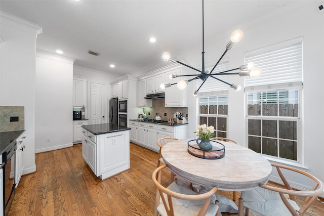 kitchen with crown molding, dark countertops, a notable chandelier, under cabinet range hood, and black appliances