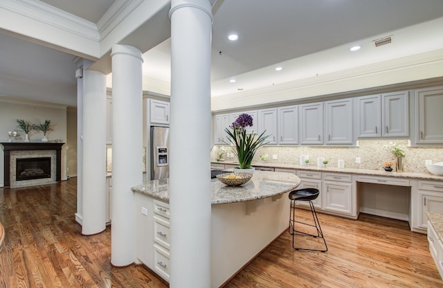 kitchen with a glass covered fireplace, stainless steel fridge, ornamental molding, visible vents, and ornate columns