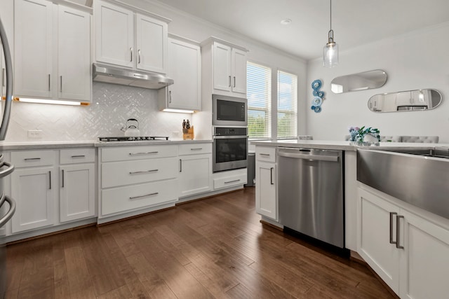 kitchen with white cabinets, light countertops, stainless steel appliances, under cabinet range hood, and ornamental molding
