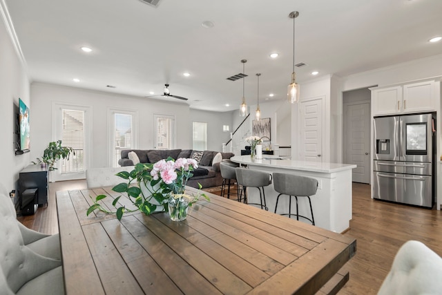 dining space featuring visible vents, ornamental molding, dark wood-style flooring, stairway, and a ceiling fan
