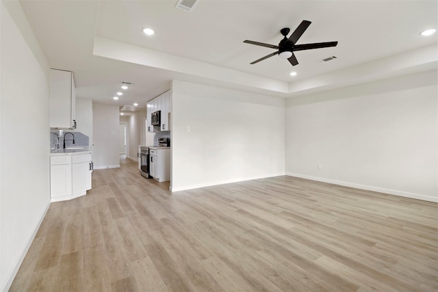 unfurnished living room with a tray ceiling, recessed lighting, ceiling fan, light wood-type flooring, and baseboards