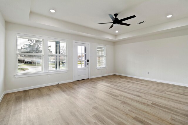unfurnished room featuring a tray ceiling, healthy amount of natural light, light wood-style flooring, baseboards, and recessed lighting