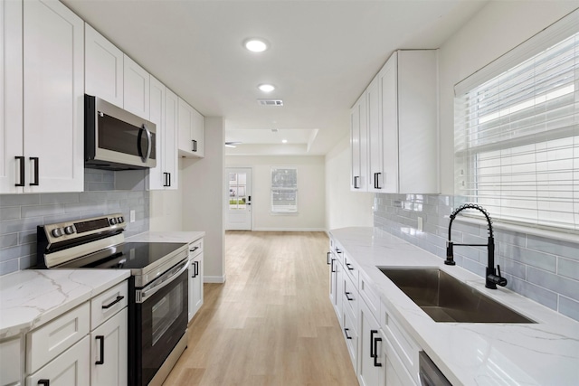 kitchen with appliances with stainless steel finishes, a sink, light wood-type flooring, decorative backsplash, and recessed lighting