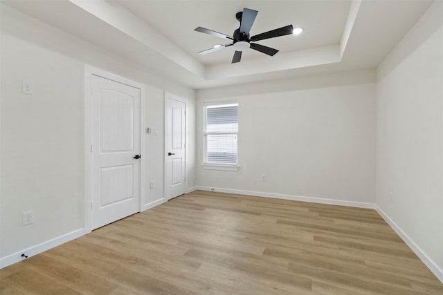 unfurnished bedroom featuring light wood-style floors, a raised ceiling, baseboards, and a ceiling fan
