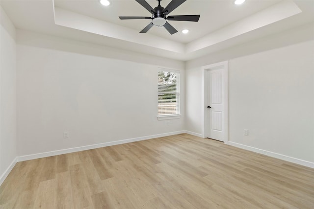 spare room with a tray ceiling, light wood-type flooring, recessed lighting, baseboards, and a ceiling fan