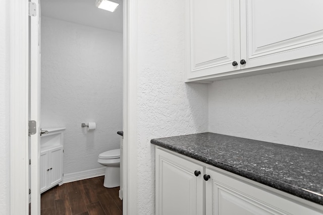 bathroom with wood finished floors, vanity, a textured wall, baseboards, and toilet