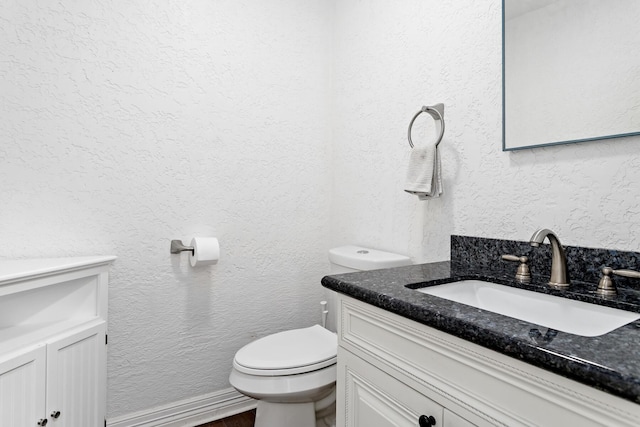 bathroom featuring toilet, a textured wall, vanity, and wood finished floors