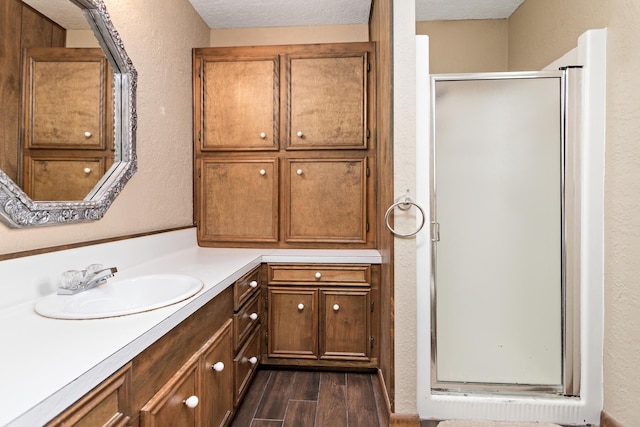 full bathroom featuring a shower stall, vanity, a textured wall, and wood finished floors