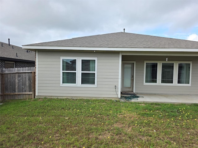 rear view of house featuring fence, a lawn, a shingled roof, and a patio