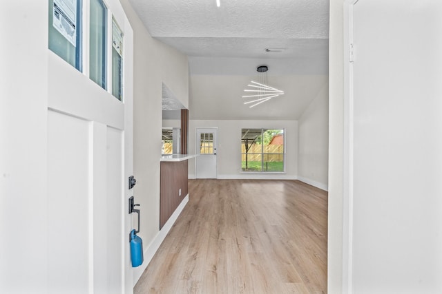 entryway with a notable chandelier, a textured ceiling, light wood-type flooring, baseboards, and lofted ceiling