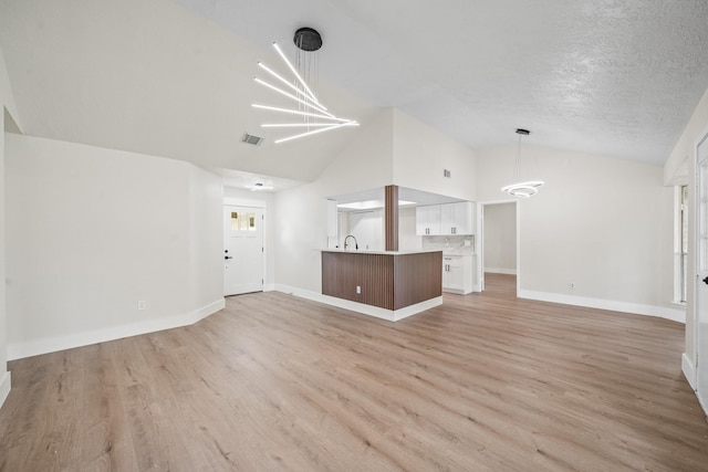 unfurnished living room featuring light wood-style flooring, baseboards, visible vents, a chandelier, and lofted ceiling