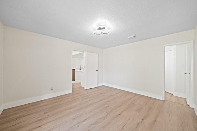 spare room with a textured ceiling, a sink, light wood-type flooring, baseboards, and visible vents
