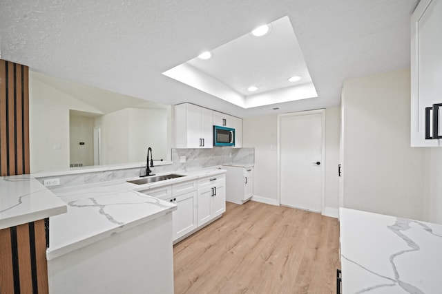 kitchen with light stone counters, a sink, light wood-type flooring, a raised ceiling, and white cabinetry