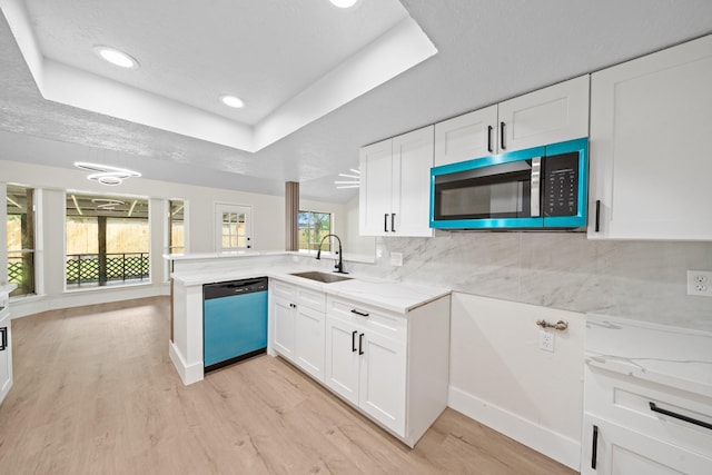 kitchen featuring a sink, dishwasher, light wood finished floors, a raised ceiling, and stainless steel microwave