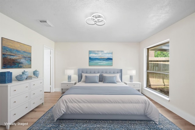 bedroom featuring a textured ceiling, light wood-type flooring, visible vents, and baseboards