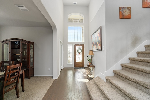 foyer featuring a high ceiling, wood finished floors, visible vents, arched walkways, and stairs