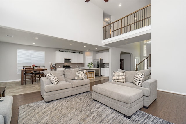 living room featuring arched walkways, light wood-type flooring, a ceiling fan, and baseboards