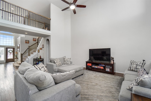 living area with a high ceiling, wood finished floors, arched walkways, stairs, and ceiling fan