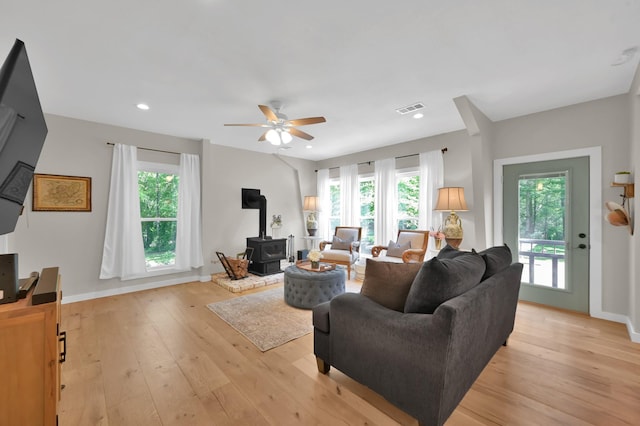 living room featuring a wood stove, light wood-style flooring, visible vents, and a wealth of natural light