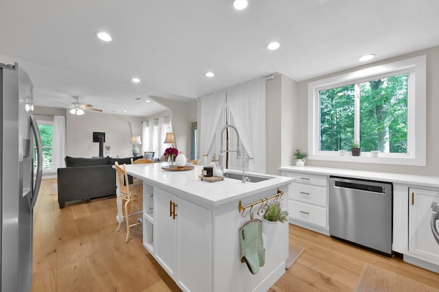 kitchen featuring stainless steel appliances, a sink, light wood-style floors, a center island with sink, and white cabinetry