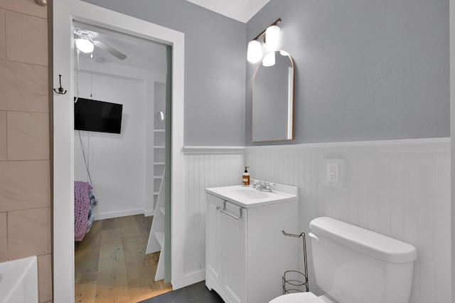 full bathroom featuring toilet, wainscoting, wood finished floors, ceiling fan, and vanity