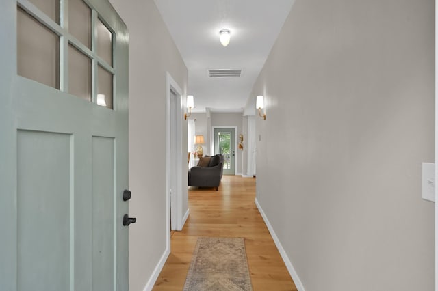 corridor featuring baseboards, light wood finished floors, and visible vents