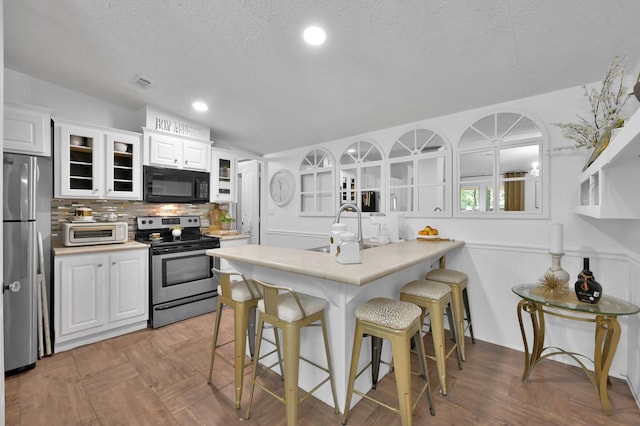 kitchen with a sink, white cabinetry, glass insert cabinets, a breakfast bar, and appliances with stainless steel finishes