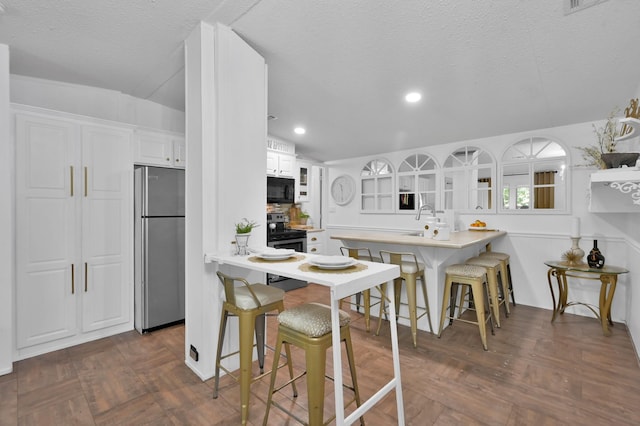 kitchen with stainless steel appliances, a breakfast bar, a peninsula, glass insert cabinets, and white cabinetry