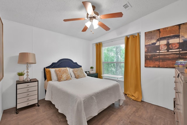 bedroom with wood finished floors, visible vents, a textured ceiling, and ceiling fan