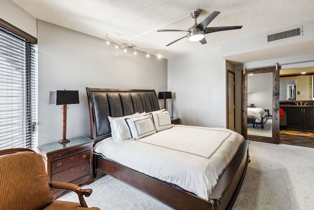 carpeted bedroom featuring track lighting, a barn door, ceiling fan, visible vents, and a textured ceiling