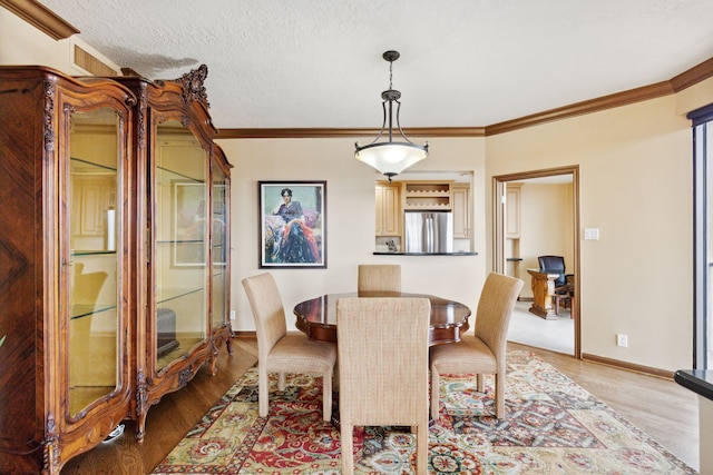 dining space with a textured ceiling, wood finished floors, crown molding, and baseboards