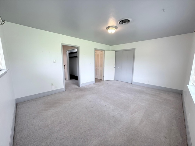 unfurnished bedroom with multiple closets, visible vents, baseboards, and light carpet
