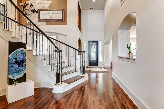 entryway with a towering ceiling, wood finished floors, baseboards, and arched walkways